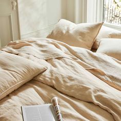 an open book sitting on top of a bed next to pillows and blankets in front of a window