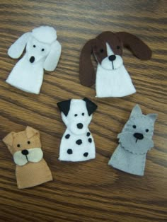 four felt dogs sitting on top of a wooden table next to each other and one dog is wearing a white shirt with black spots