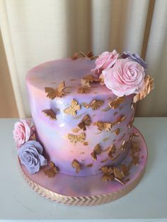 a pink and purple cake with gold butterflies on the top is sitting on a table