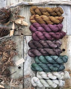 several skeins of yarn sitting on top of a wooden table next to pine cones