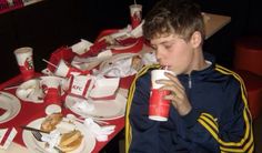 a young man sitting at a table with plates and cups in front of him eating food