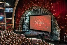 an auditorium full of people watching oscars on the big screen in front of them