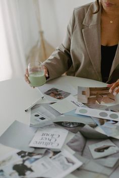 a woman sitting at a table covered in photos and papers with a glass of green liquid