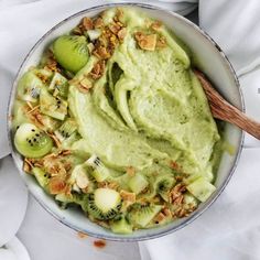 a bowl filled with kiwi and nuts on top of a white cloth next to a wooden spoon