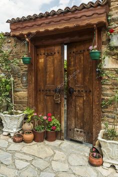 two wooden doors with potted plants in front of them on a stone patio area