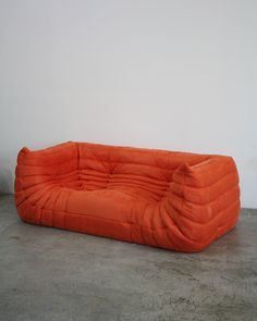 an orange couch sitting on top of a cement floor