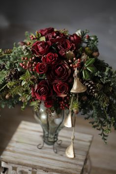 a vase filled with red roses and greenery on top of a wooden table next to a bell