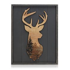 a wooden deer head with trees on it's back wall hanging in a black frame