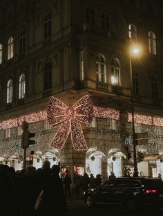 a large bow is lit up on the side of a building with people walking around it