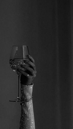 a hand holding a wine glass in front of a black and white photo with water droplets on it