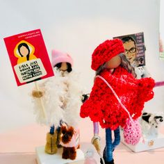 there are two dolls on the table with one holding a sign and another wearing a red coat