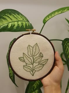 a person holding up a small embroideryed plant in front of a green leafy background