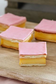 four pieces of cake sitting on top of a wooden cutting board with pink icing