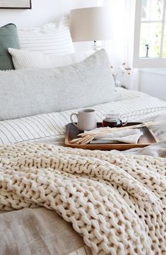 a bed covered in blankets and pillows next to a window with a cup on it