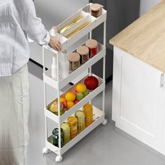 a woman standing next to a white cart filled with fruits and vegetables on top of a kitchen counter