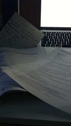 an open laptop computer sitting on top of a desk next to papers and paperwork in front of it