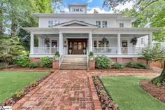 a large white house with brick walkway leading to the front door and steps up to it