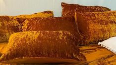 a bed covered in gold velvet pillows and blankets