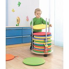 a young boy standing on top of a stack of colorful discs in a room filled with furniture