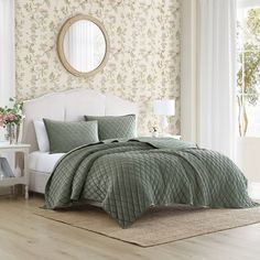 a bed with green comforter and pillows in a room next to a mirror on the wall