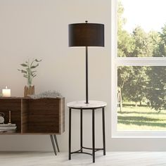 a table with a lamp on it in front of a window and a cabinet next to it