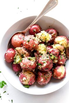 a white bowl filled with red potatoes covered in herbs and topped with a silver spoon