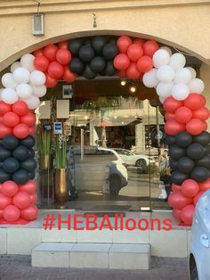 an arch made out of balloons in front of a building with cars parked outside it