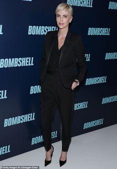 a woman standing in front of a wall wearing a black suit and high heeled shoes