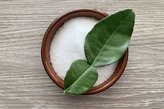 a bowl filled with sugar and two green leaves on top of it next to a wooden table