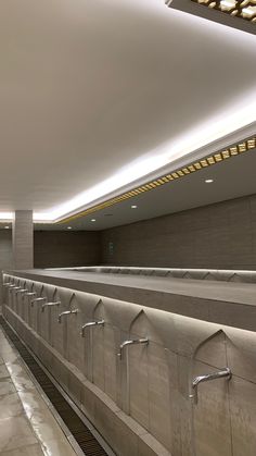 an empty public bathroom with no people in it and lights on the ceiling over the urinals