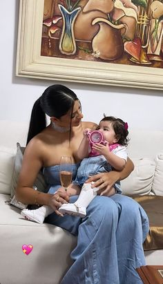 a woman sitting on a couch holding a baby and drinking from a wine glass in her mouth