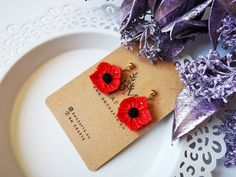 two red flowers sitting on top of a white plate next to purple leaves and paper