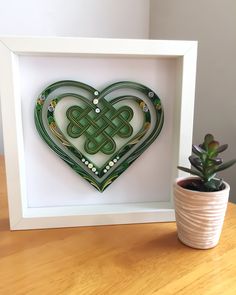 a green heart shaped artwork in a white frame next to a potted succulent