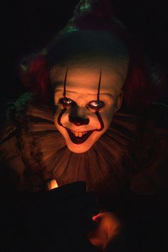 a creepy clown is looking at his cell phone in the dark with it's mouth open