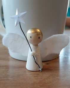 a small angel figurine holding a star on a wooden table next to a coffee cup