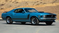 a blue muscle car parked in a parking lot next to a wall and fenced area