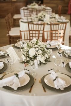 the table is set with white flowers and place settings