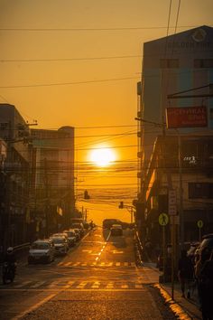 the sun is setting over a city street with cars parked on both sides and people walking down the sidewalk