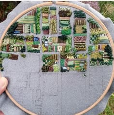 someone is holding up a cross - stitch pattern in front of some plants and trees