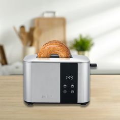 a silver toaster sitting on top of a wooden table next to a bagel