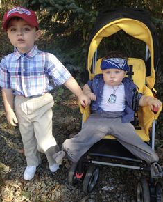 two young boys standing next to each other in front of a yellow stroller with wheels