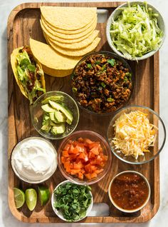 a wooden tray topped with lots of different types of food and condiments next to tortillas