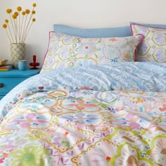 a bed with colorful sheets and pillows on top of it next to a blue dresser