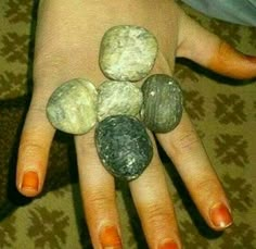 a woman's hand with four rocks on it and one is painted orange, the other is white