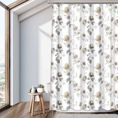 a white shower curtain with flowers on it next to a wooden table and window sill