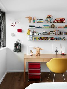 a room with a desk, chair and shelves filled with toys on the wall above it