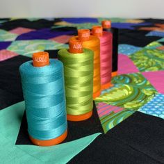 three spools of thread sitting on top of a quilting material covered table