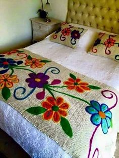 a white bed topped with lots of pillows and colorful flowers on it's cover