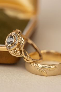 two gold wedding rings sitting on top of each other next to a green case with a diamond in it