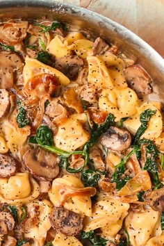 pasta with mushrooms, spinach and cheese in a pan on a wooden table top